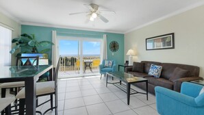 A living room with a balcony, a ceiling fan, a TV, and a dining area.