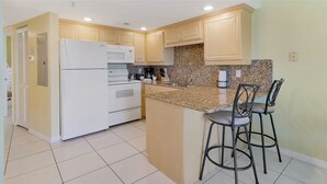 A kitchen with a refrigerator, oven, microwave, granite countertop, and two bar stools.