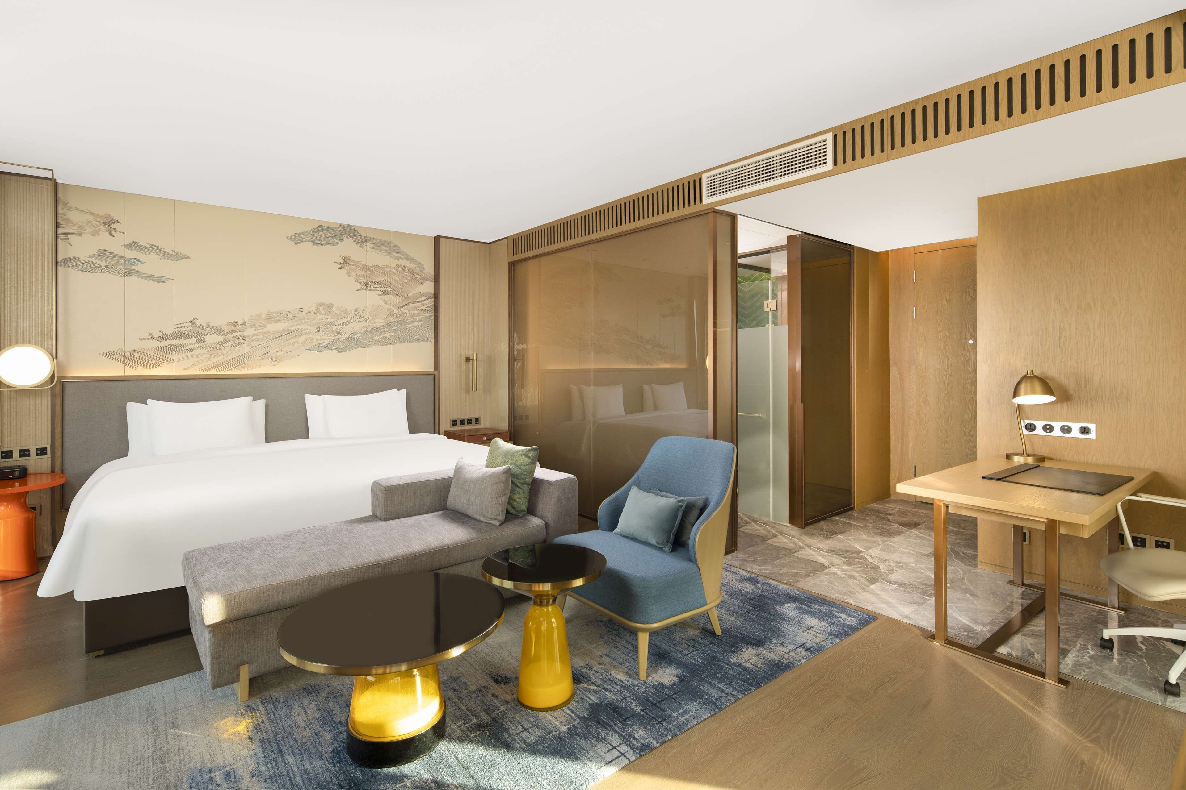 Una habitación de hotel moderna con una cama grande, un escritorio, un sillón azul y una pequeña mesa redonda.