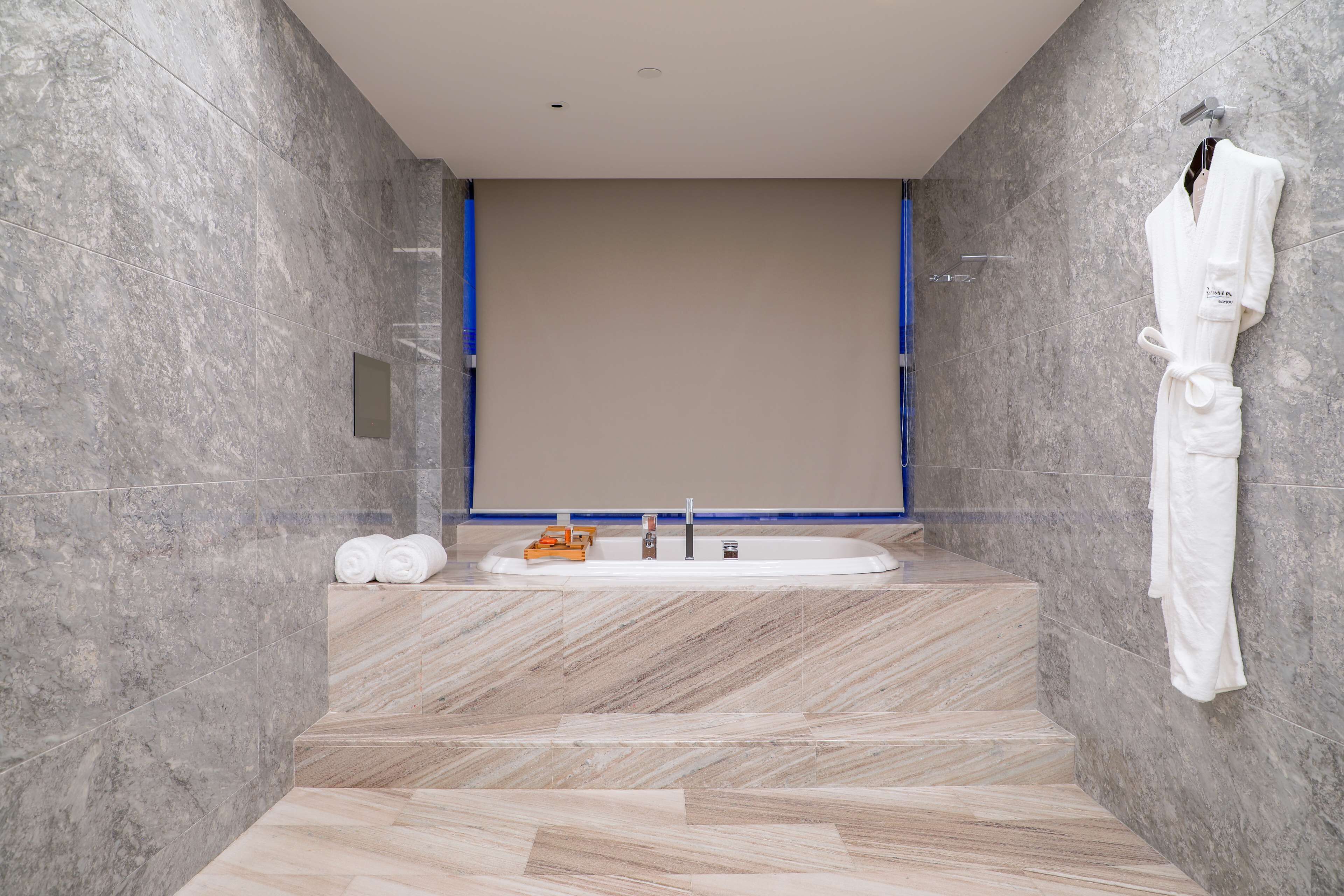 A modern bathroom with a marble floor, a large bathtub, and a white robe hanging on the wall.