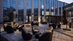 An outdoor seating area with wicker furniture and a bar, in front of a modern building with reflective glass windows. - Radisson Suzhou (Suzhou)
