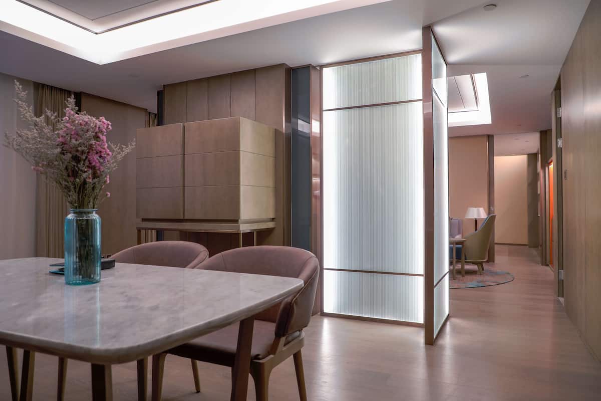 A modern hotel room with a dining area, a large cabinet, and a view through a sliding door.
