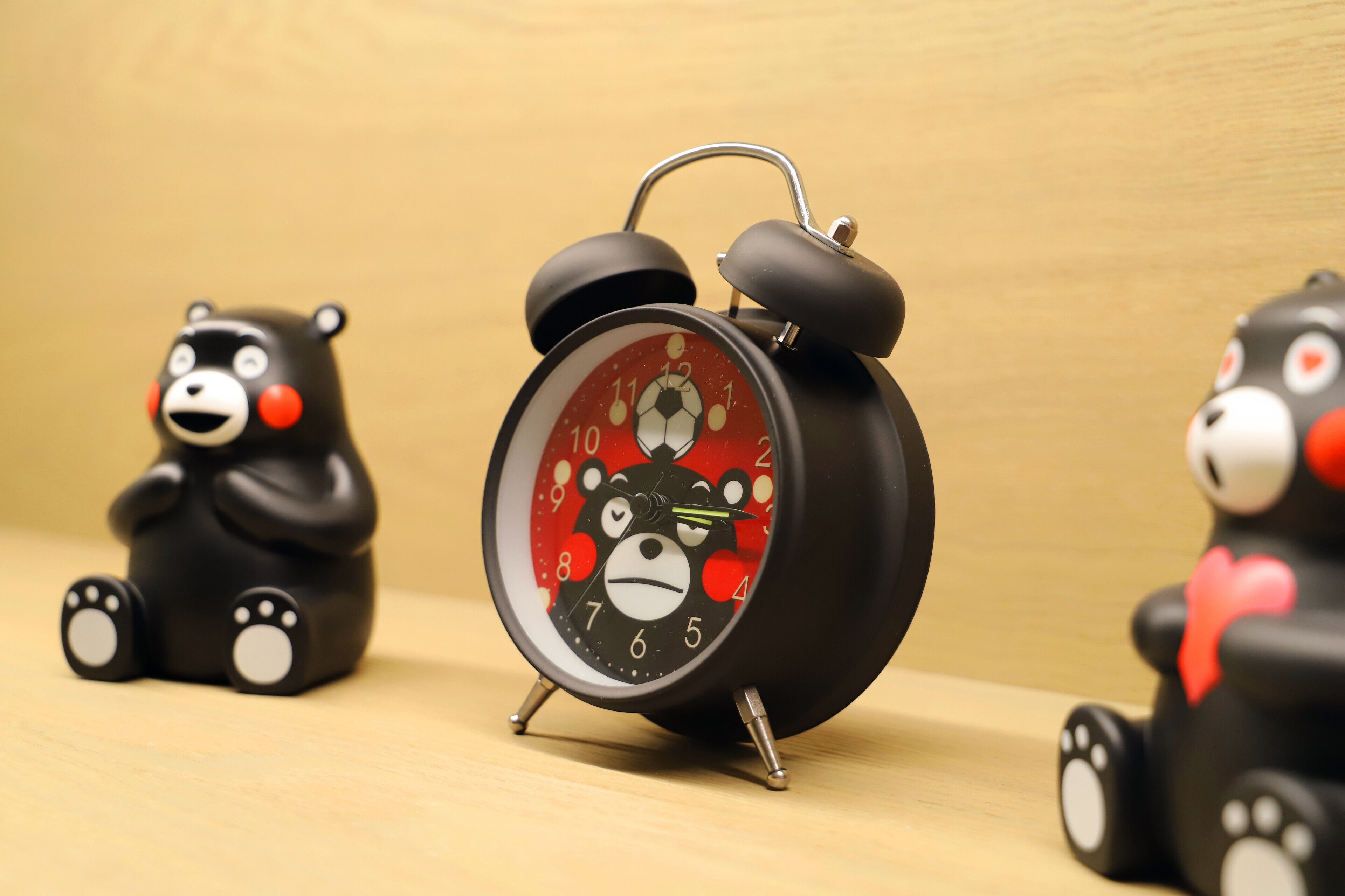 A black alarm clock with a bear face on the dial, surrounded by two bear figurines.