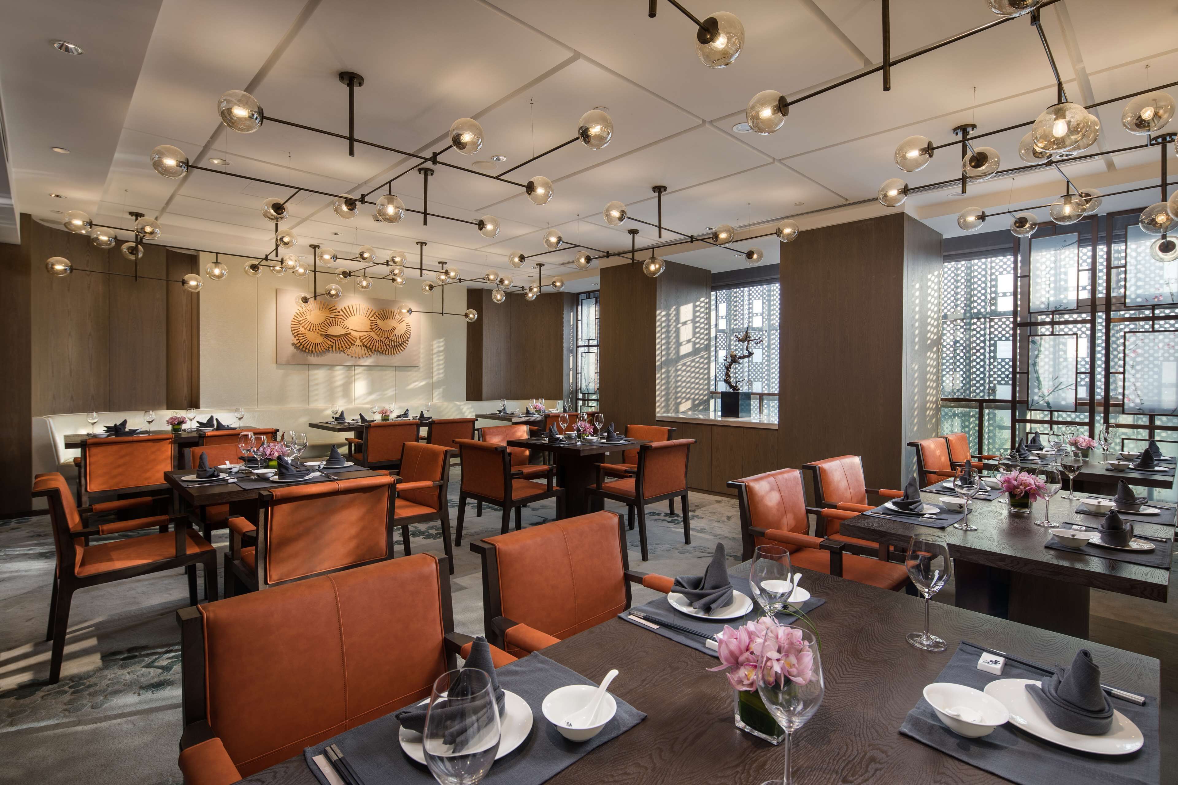 A modern restaurant with multiple dining tables and chairs, overhead lighting, and large windows.