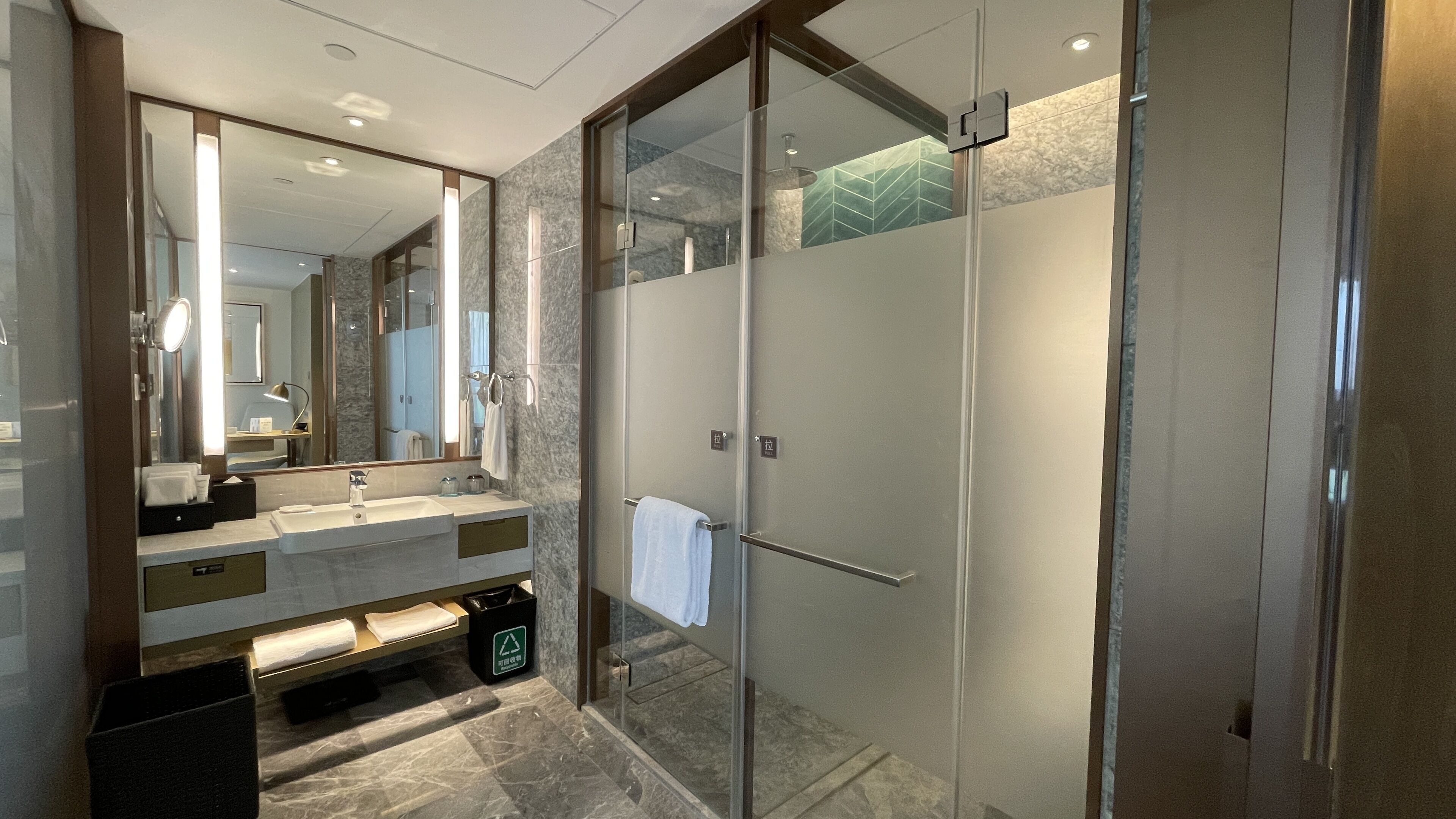 A modern bathroom with a glass-enclosed shower, a large mirror, and a marble countertop.