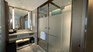A modern bathroom with a glass-enclosed shower, a large mirror, and a marble countertop.