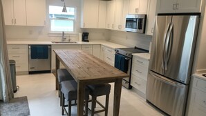Eine moderne Küche mit weißen Schränken, Edelstahlgeräten, einem Holztisch und Barhocker.