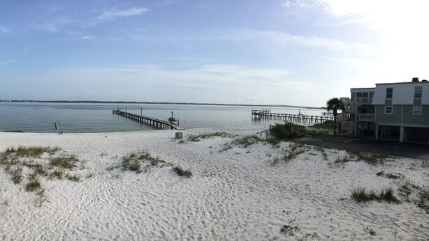 Ein Strand mit einem Steg, der sich in ruhiges Wasser erstreckt, einem Rettungsschwimmturm und einem Gebäude mit einem Balkon.