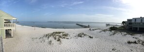 Une plage avec une jetée qui s’avance dans des eaux calmes, un poste de surveillance pour les sauveteurs et un bâtiment doté d’un balcon.