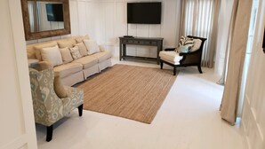 Ein Wohnzimmer mit einer Couch, einem Sessel und einem an der Wand befestigten Fernseher.