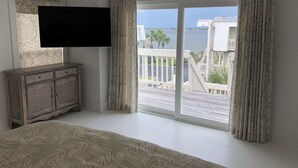 Ein Schlafzimmer mit einem großen Bett, einem an der Wand montierten Fernseher und einem Balkon mit Blick auf das Meer und Gebäude.