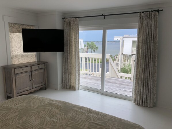 Une chambre avec un grand lit, un téléviseur fixé au mur et un balcon offrant une vue sur la mer et les bâtiments.