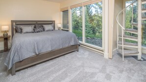 Un dormitorio con una cama grande, una mesita de noche, una ventana con vistas a árboles y una escalera en espiral.