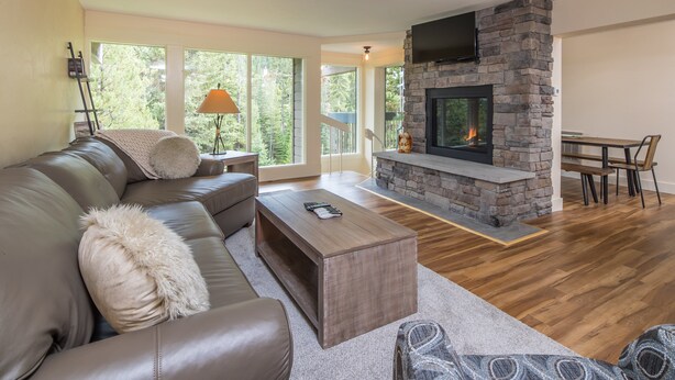 Una sala de estar moderna con chimenea de piedra, sofá de cuero y comedor con piso de madera.