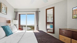 A hotel room with a bed, a dresser, a large mirror, and a balcony with a view of the ocean. - Surf Beach 406 - Luxury Corner Unit (Treasure Island)