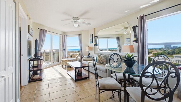 A spacious living area with a balcony overlooking the beach, furnished with a sofa, chairs, and a dining table. - Surf Beach 406 - Luxury Corner Unit (Treasure Island)