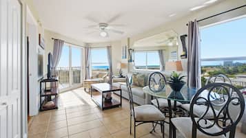 A spacious living area with a balcony overlooking the beach, furnished with a sofa, chairs, and a dining table.