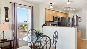 A modern kitchen with wooden cabinets, stainless steel appliances, and a glass dining table. - Surf Beach 406 - Luxury Corner Unit (Treasure Island)