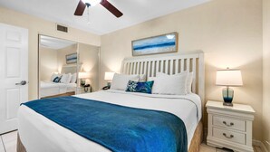 Habitación de hotel con cama, mesitas de noche, ventilador de techo y un cuadro en la pared.