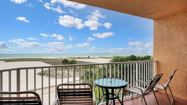 A balcony with a glass table and chairs, overlooking a beach with clear skies. - Surf Beach 405 - Spectacular Sunsets - Beach Front (Treasure Island)