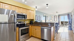 A modern kitchen with stainless steel appliances, wooden cabinets, and a granite countertop. - Surf Beach 405 - Spectacular Sunsets - Beach Front (Treasure Island)