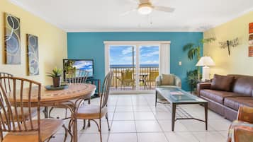 Un salon comprenant un coin repas, un téléviseur et un balcon avec vue sur l’océan.