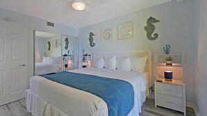 Een slaapkamer met een groot bed, een nachtkastje met een lamp en een wandplank met decoratieve objecten.