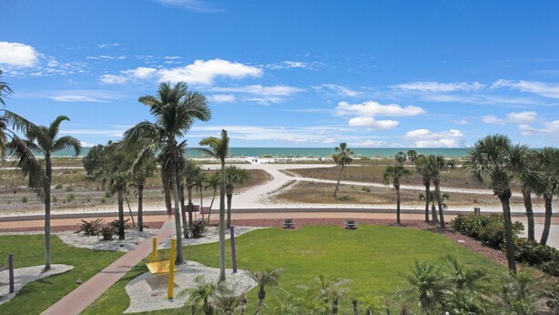Vista de playa con palmeras, un camino y una zona costera distante.