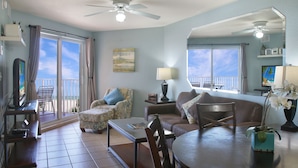 A living room with a sofa, armchair, table, and chairs. There is a TV, a lamp, and a plant on the table. - Surf Beach 402 - Spectacular Sunsets - Beach Front (Treasure Island)