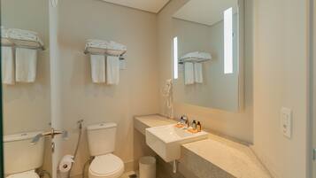 A bathroom with two toilets, a sink, a mirror, and towels on a rack.