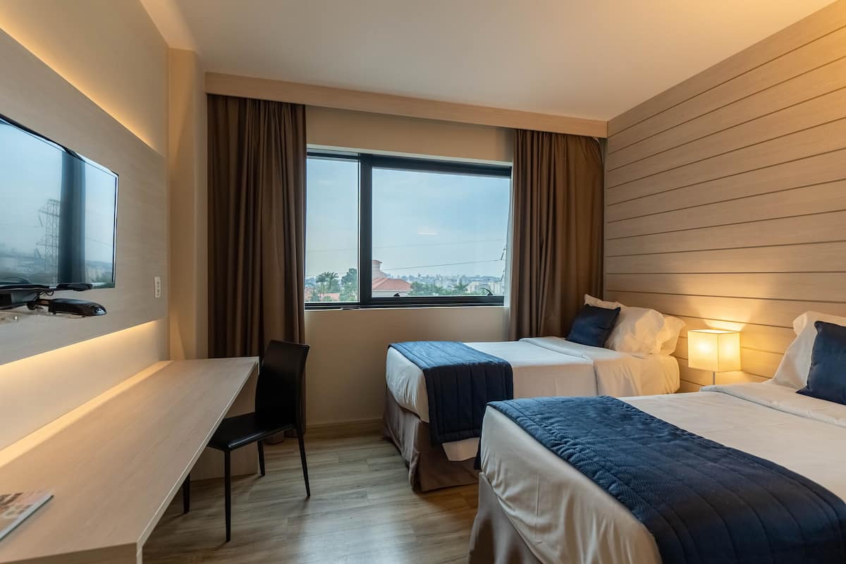 Une chambre d’hôtel avec deux lits, un bureau, une chaise et un téléviseur.