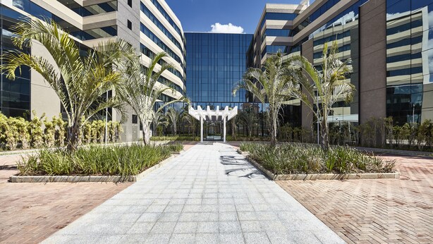 A modern building complex with a central pathway flanked by palm trees and planters. - Hotel Contemporâneo BY Royal Palm Hotels & Resorts (Campinas)