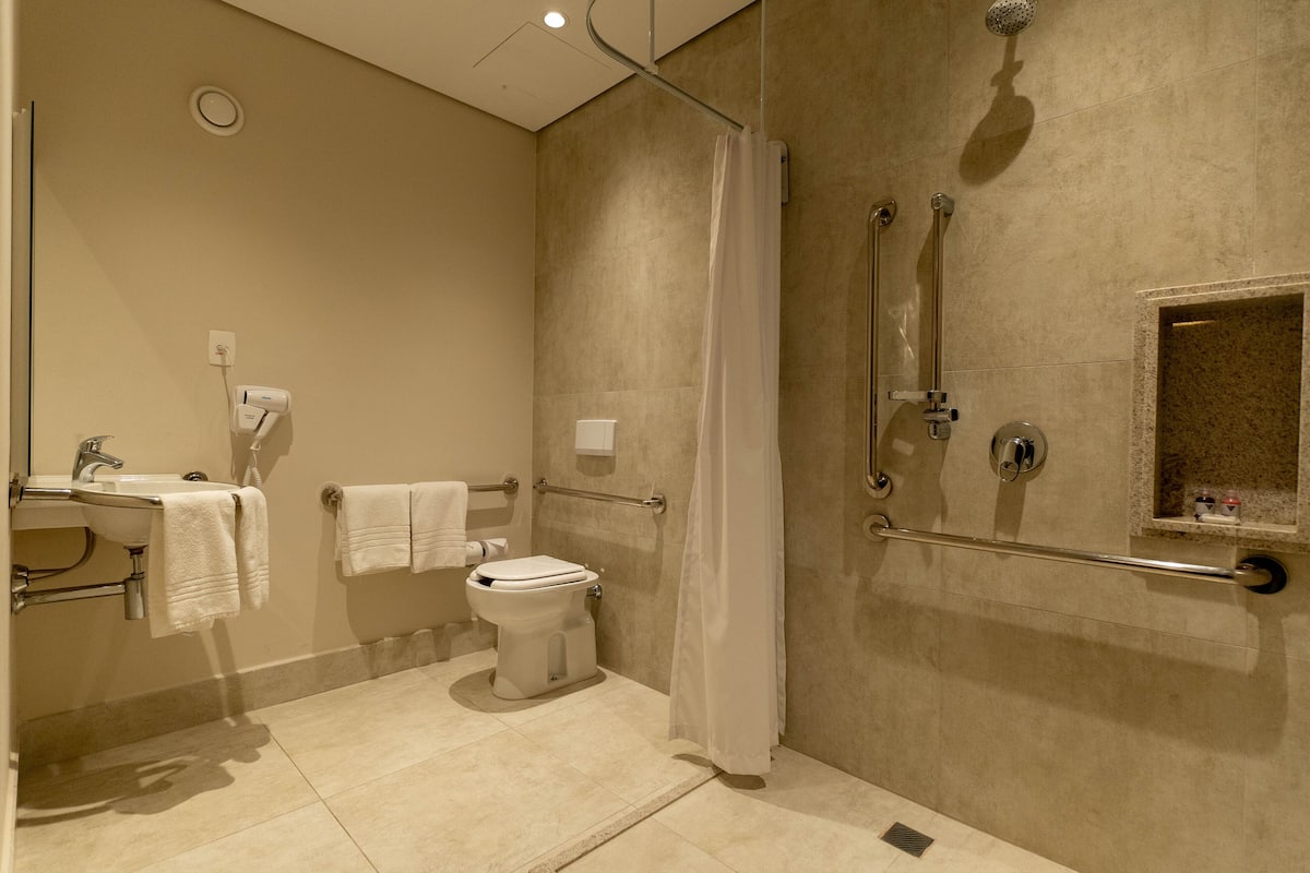 Une salle de bain moderne équipée de toilettes, d’un lavabo et d’une zone de douche, comprenant des barres d’appui et un sèche-mains.