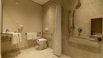 A modern bathroom with a toilet, sink, and shower area, including grab bars and a hand dryer.