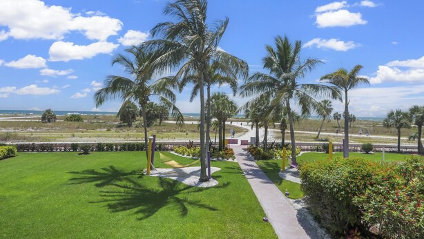 A well-maintained lawn with palm trees, a pathway, and a view of the beach and ocean.