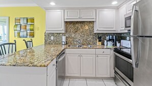 A kitchen with white cabinets, granite countertops, stainless steel appliances, and a yellow accent wall.