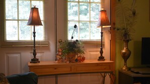 Una habitación con un escritorio de madera, dos lámparas, un florero con flores y una estantería.