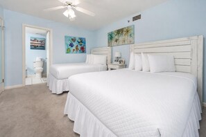 A bedroom with two beds, a ceiling fan, and artwork on the walls.