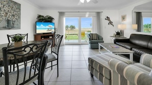 Ein Wohnzimmer mit Essbereich, einer Couch, einem Fernseher und einem Balkon mit Blick auf den Strand.