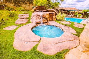 Un patio trasero con piscina, una cascada pequeña y una pérgola.