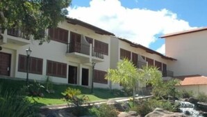 A resort with a pool surrounded by rocks and greenery, a white building with balconies, and a clear blue sky. - Hotel Dom Otto (Vespasiano)