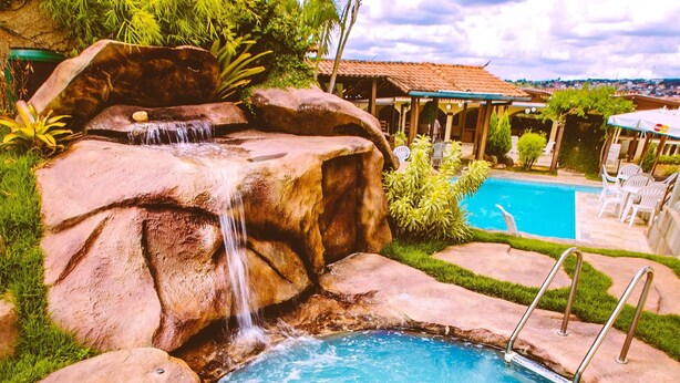 A swimming pool with a waterfall feature, surrounded by rocks and greenery. - Hotel Dom Otto (Vespasiano)