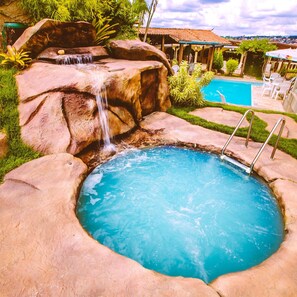 A swimming pool with a waterfall feature, surrounded by rocks and greenery. - Hotel Dom Otto (Vespasiano)