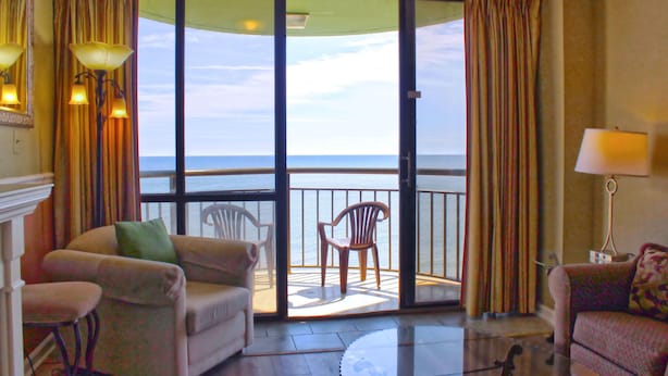 A room with a balcony, a sofa, a chair, and a lamp. - Meridian Plaza by Palmetto Vacations (Myrtle Beach)