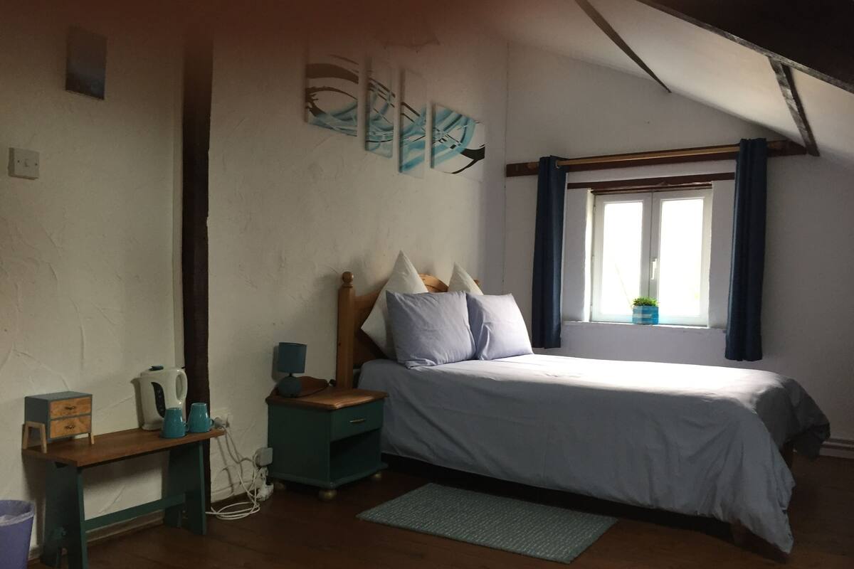 Un dormitorio con cama, mesita de noche, lámpara y ventana con cortinas.
