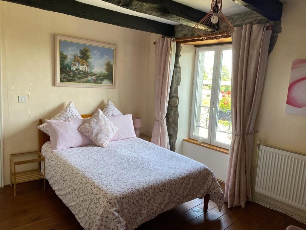 Un dormitorio con cama, una ventana con cortinas, un radiador y un cuadro en la pared.