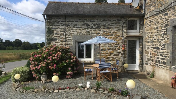 Una casa de piedra con un patio que cuenta con una mesa, sillas y una hamaca colgante, además de un gran paraguas.