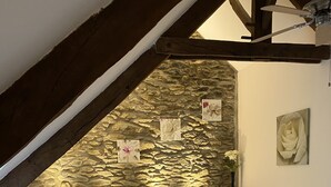 Un dormitorio con techo inclinado, pared de piedra, cama con ropa de cama blanca, dos mesitas de noche con lámparas y un cuadro en la pared.