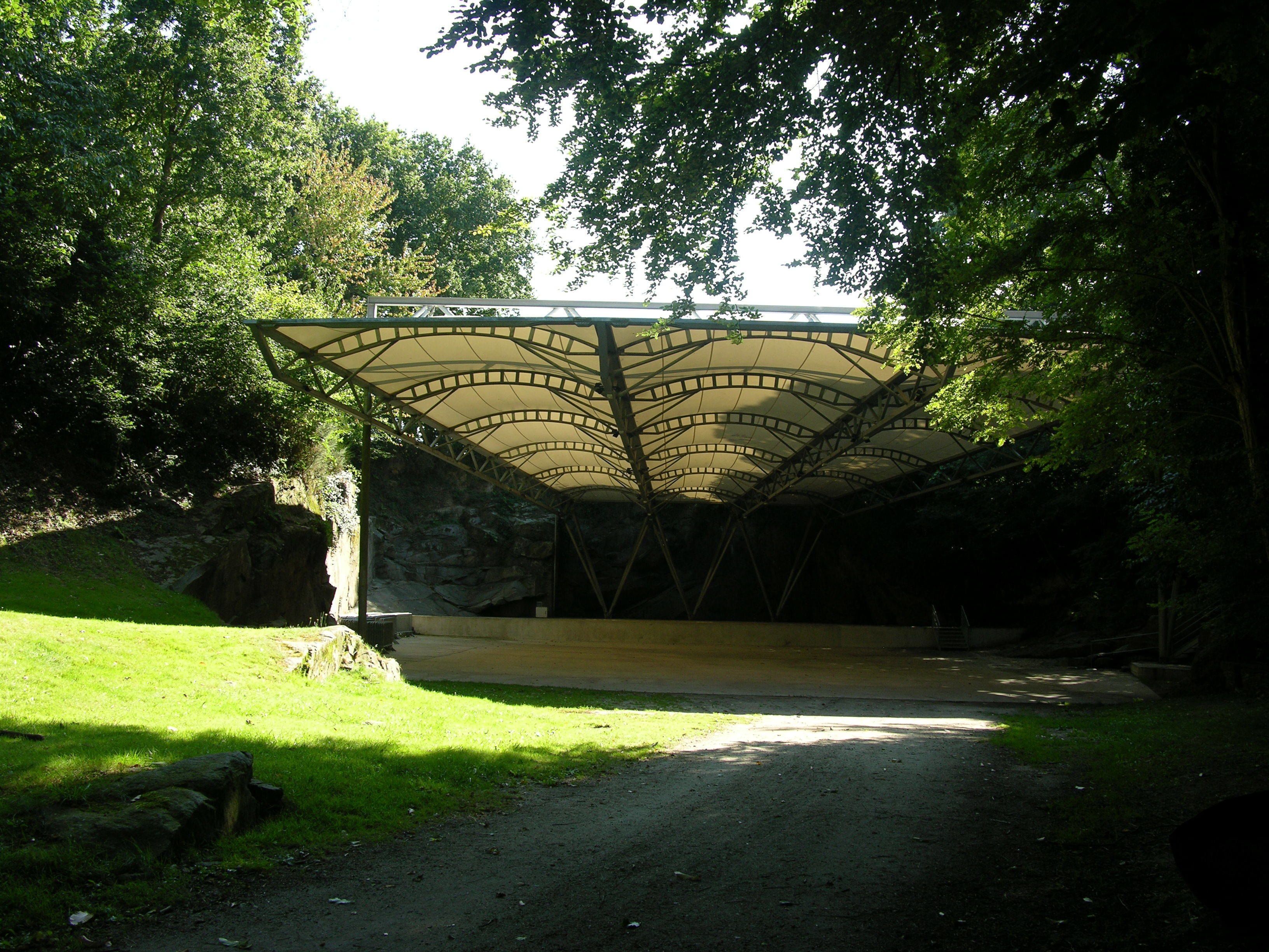 Un puente peatonal cubierto con estructura metálica y toldo, rodeado de vegetación y un sendero de tierra.