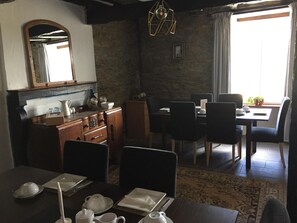 A dining area with a table set for two, a wooden cabinet with kitchenware, a mirror, and a hanging light fixture.